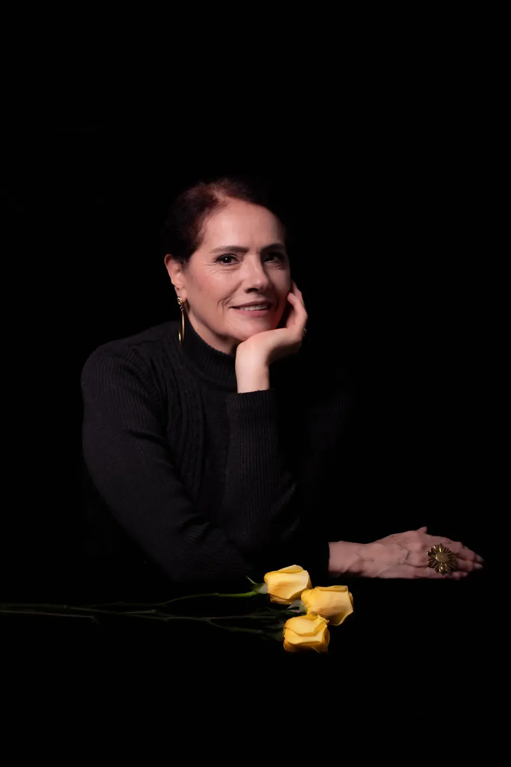 Mujer en cuello de tortuga negro con rosas amarillas sobre fondo oscuro