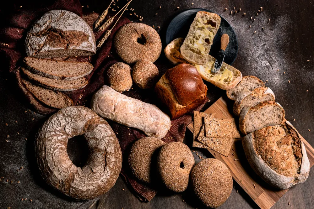 Panes rústicos artesanales con bagels, panecillos con mantequilla, panes tajados y galletas sobre superficie de madera oscura
