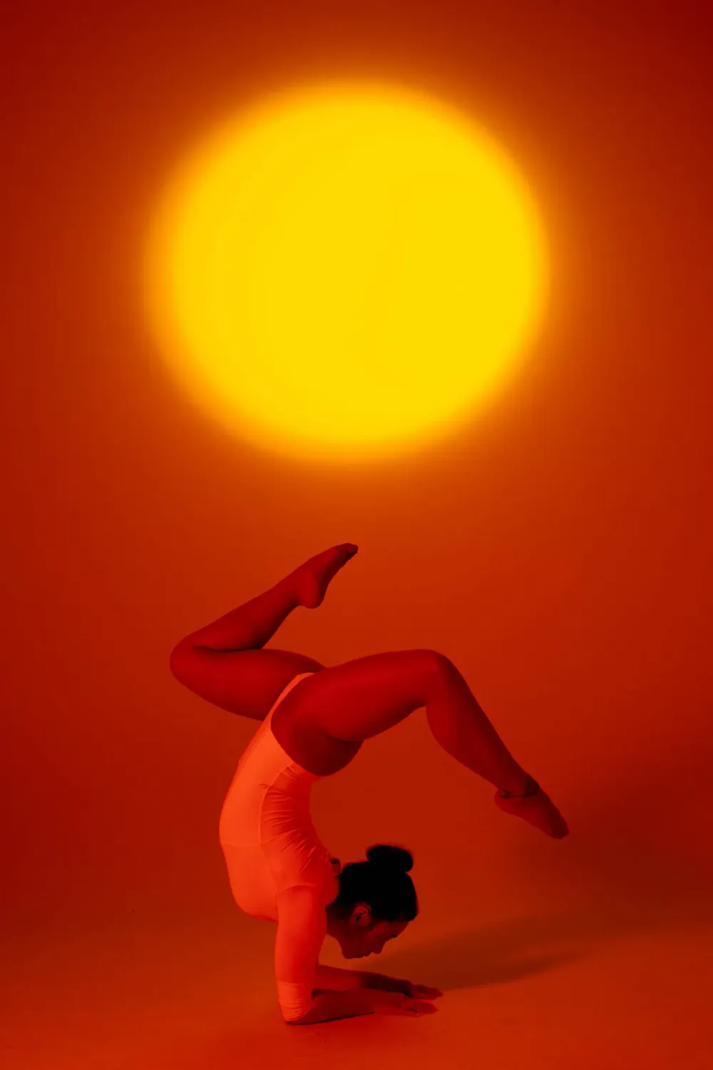Mujer realizando una postura de yoga escorpión bajo luz naranja cálida con un sol brillante de fondo